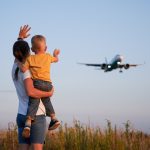 Woman with child waving hand to landing commercial airplane
