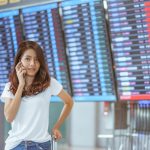woman in international airport using her mobile phone near the flight information board,